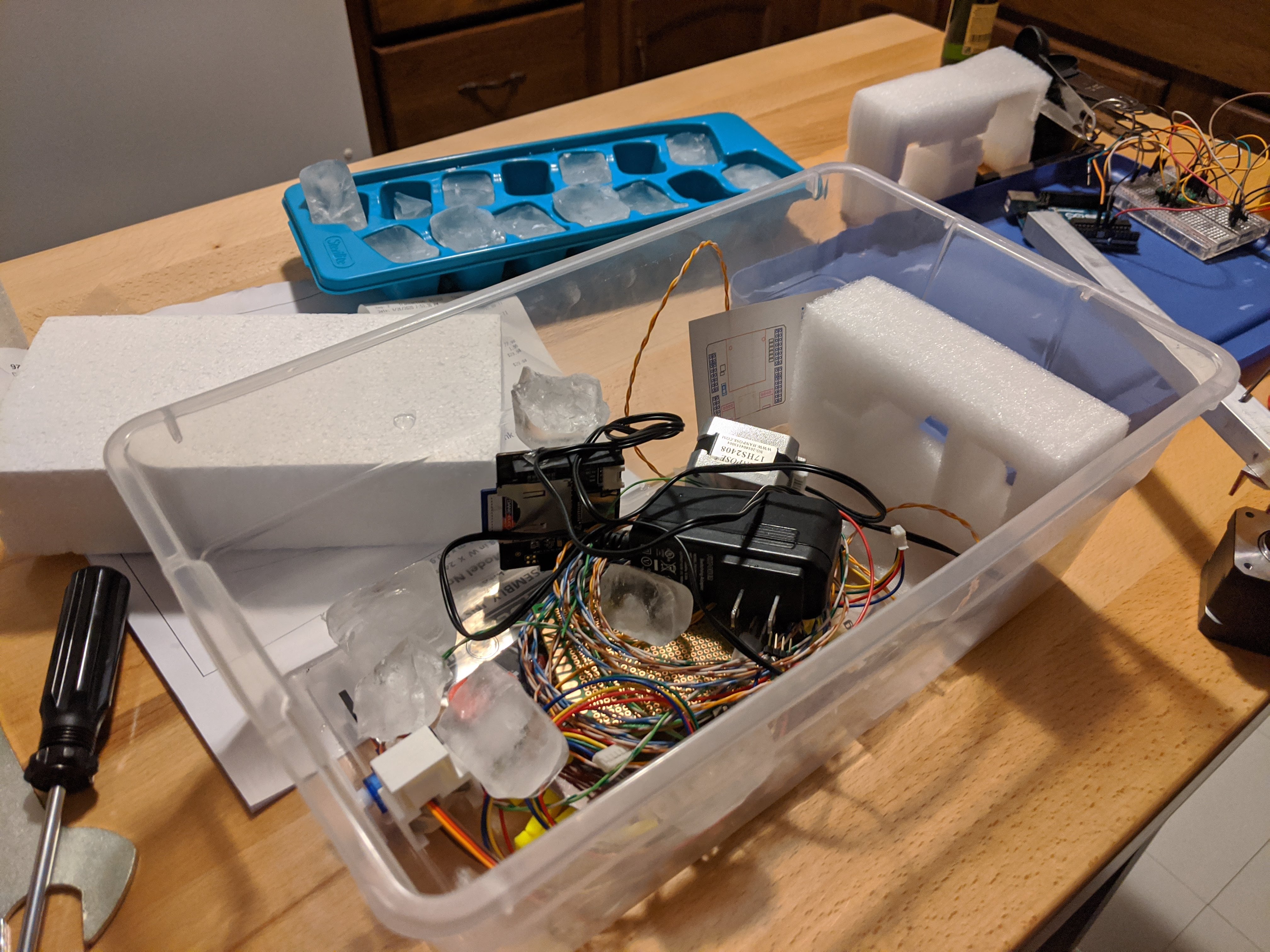 The partially disassembled arm in a plastic bin on a kitchen table. There are several ice cubes in the bin.